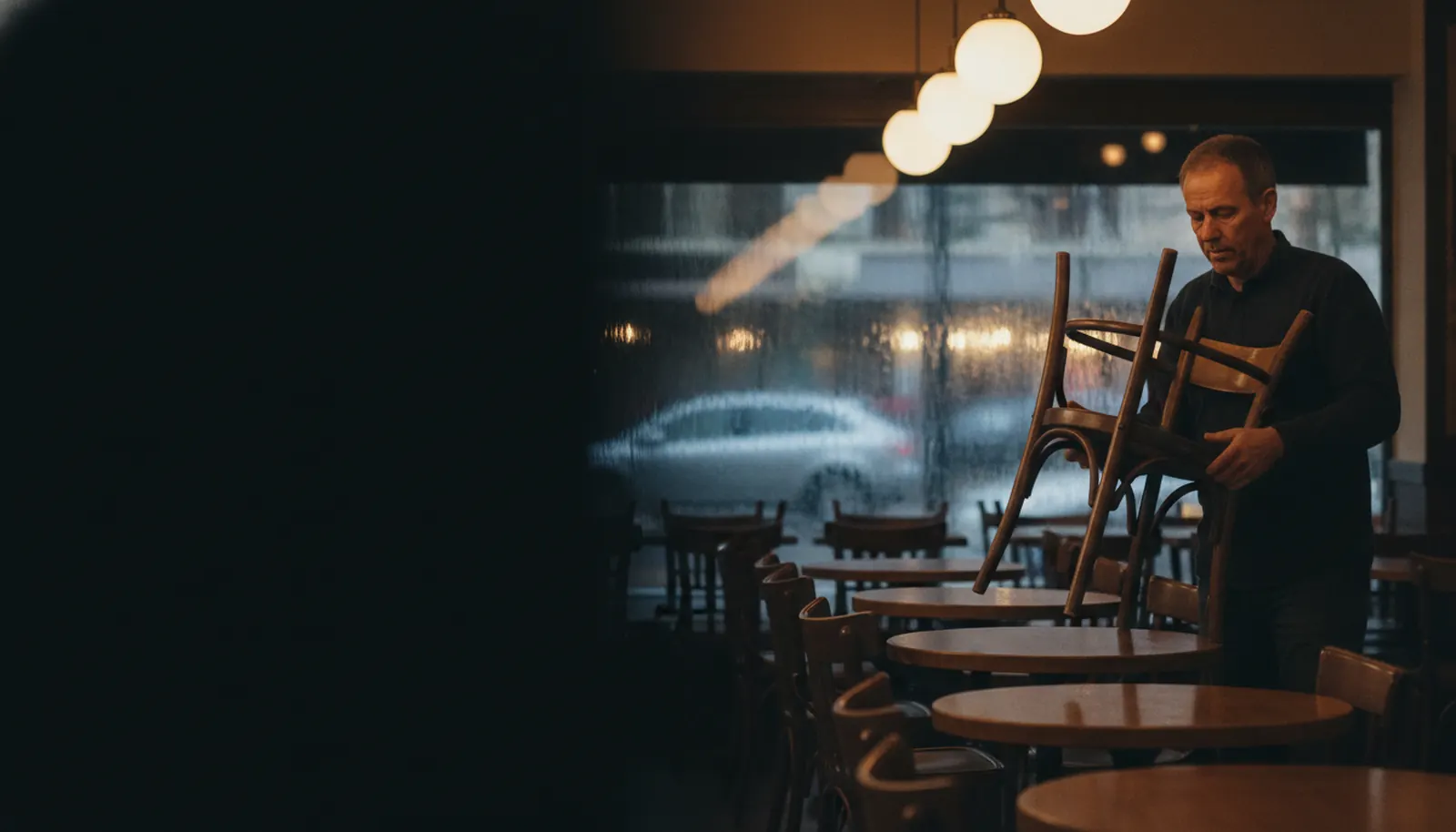 A restaurant owner stacking chairs at closing time while a new review gets an automatic thank-you reply